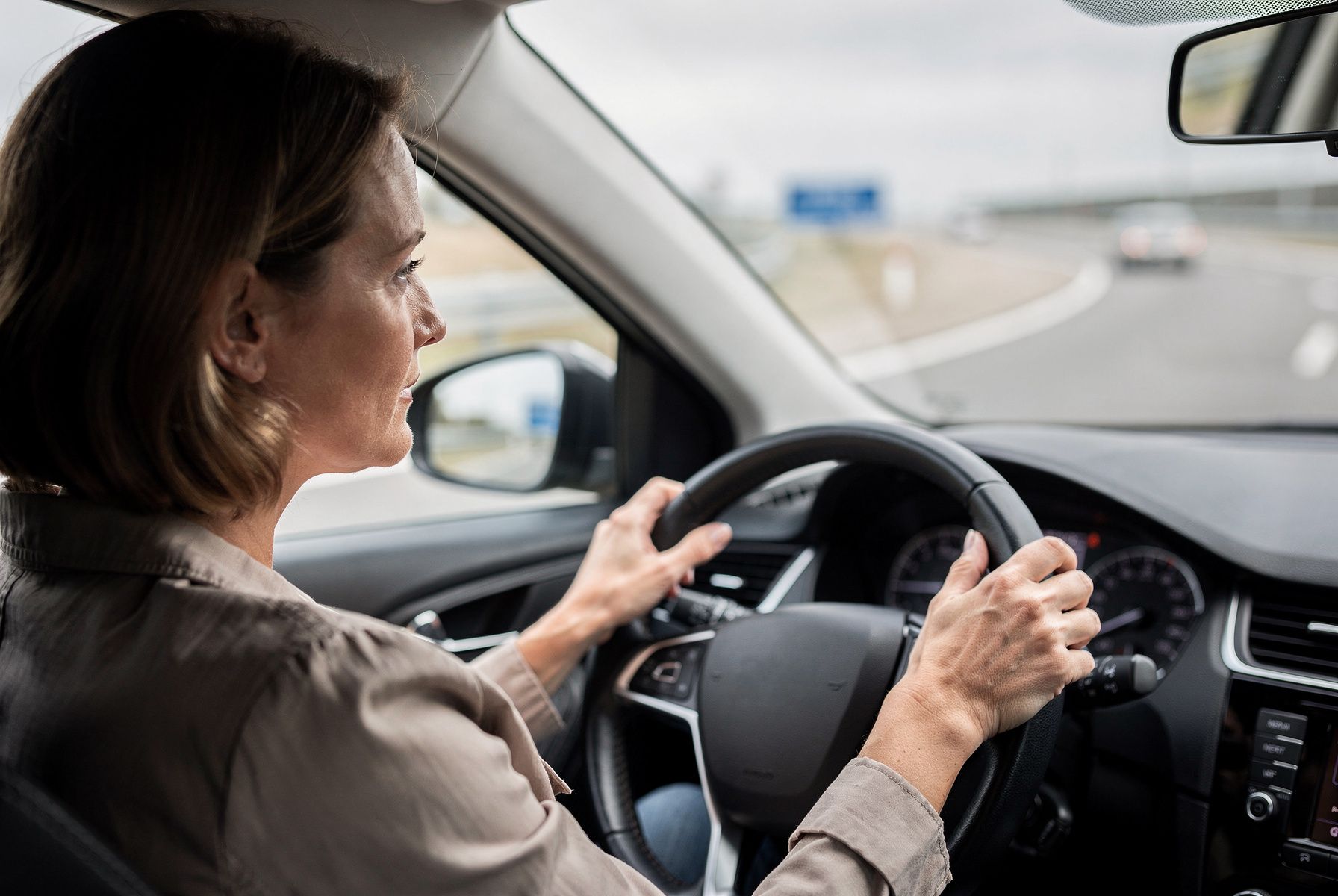 Eine Frau fährt ruhig Auto, durch die Windschutzscheibe eine Autobahnauffahrt.