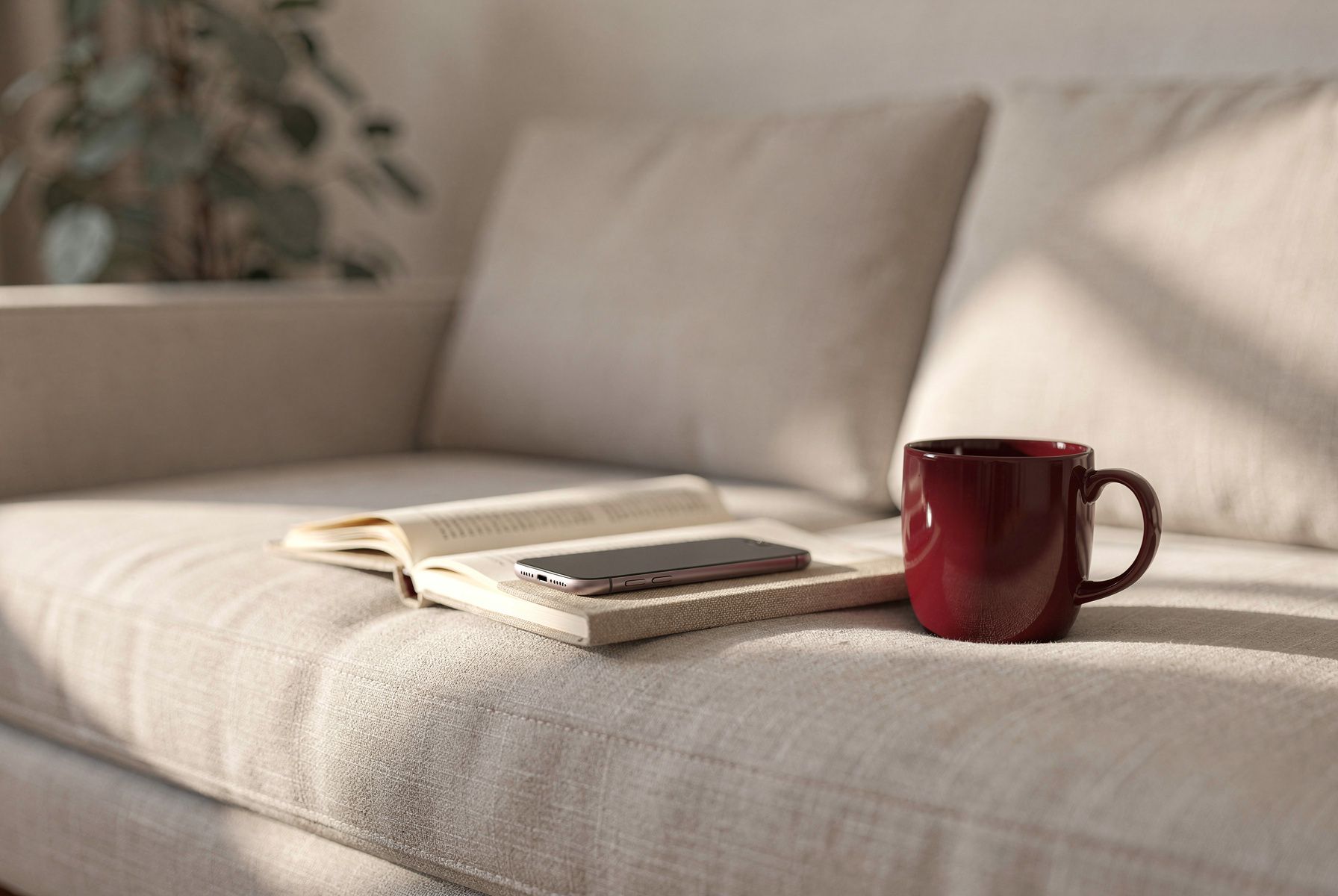 Ein umgedrehtes Handy auf dem Sofa, daneben ein offenes Buch und eine Tasse.
