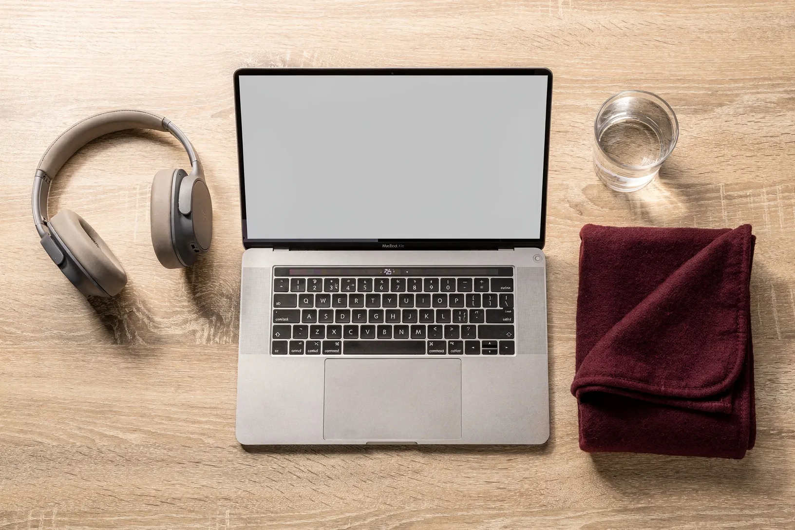 Laptop, Kopfhörer, ein Glas Wasser und eine Decke auf einem Holztisch, von oben.