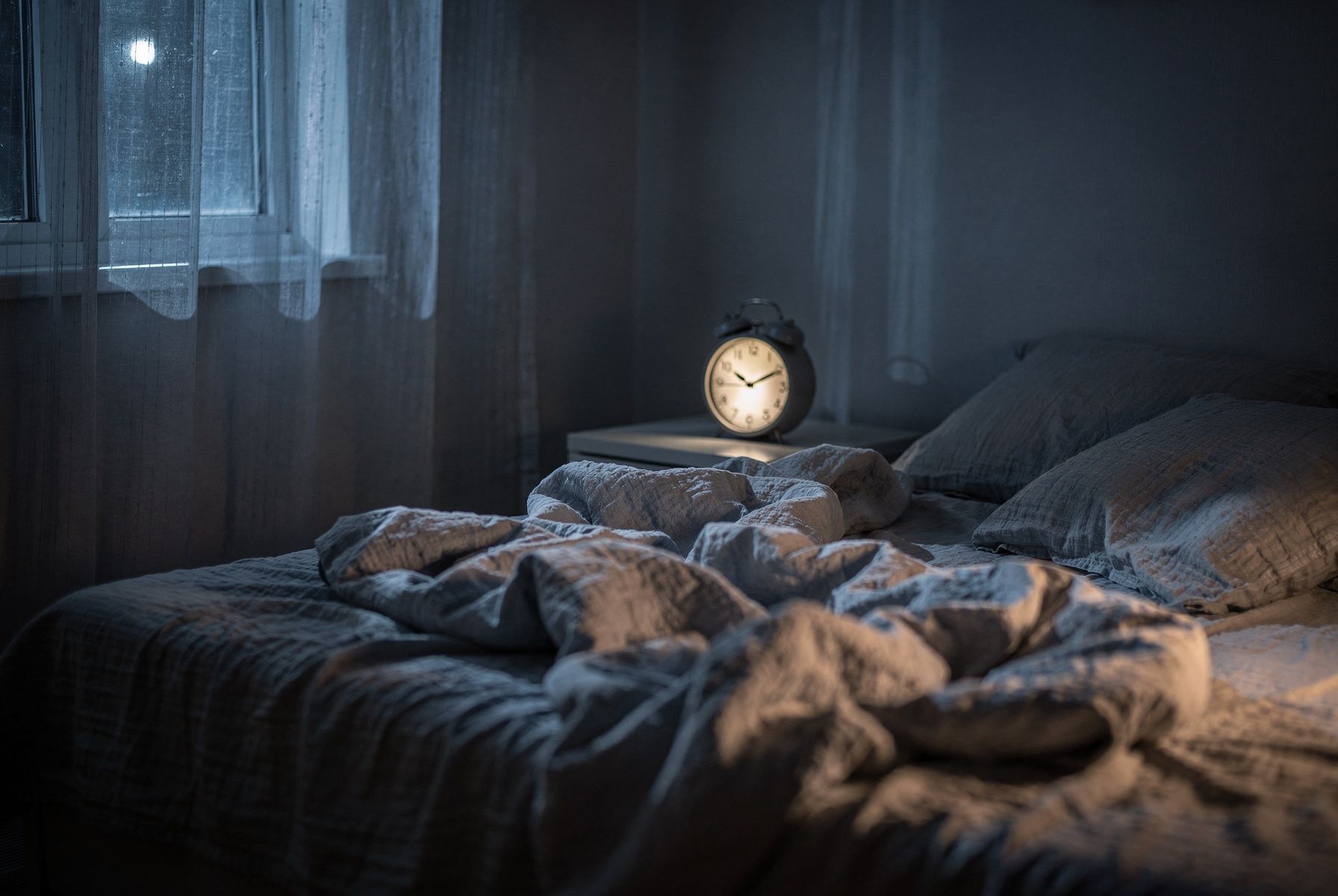 Ein Schlafzimmer in der Nacht, Mondlicht fällt aufs Bett, der Wecker zeigt 3:07.