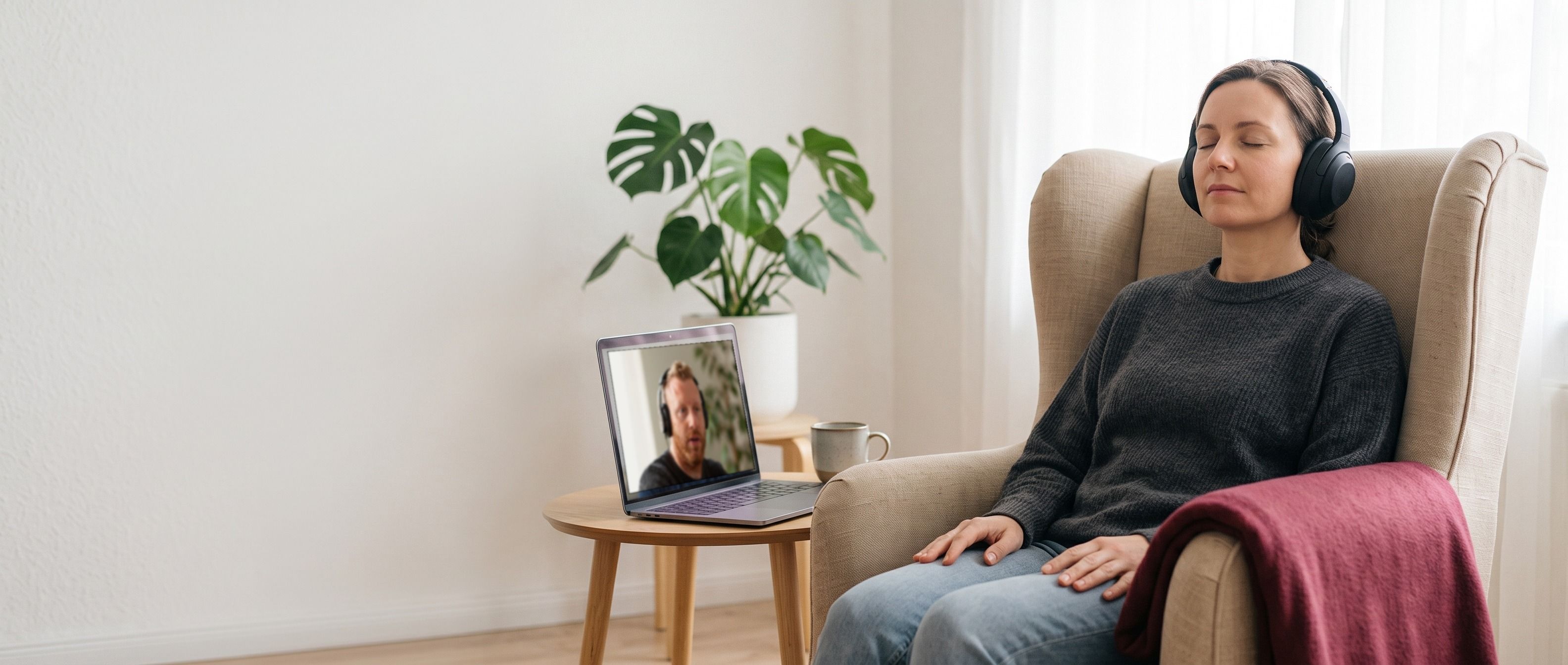 Eine Frau sitzt mit Kopfhörern und geschlossenen Augen entspannt im Sessel, daneben auf dem Laptop Tommy Müller im Videocall.