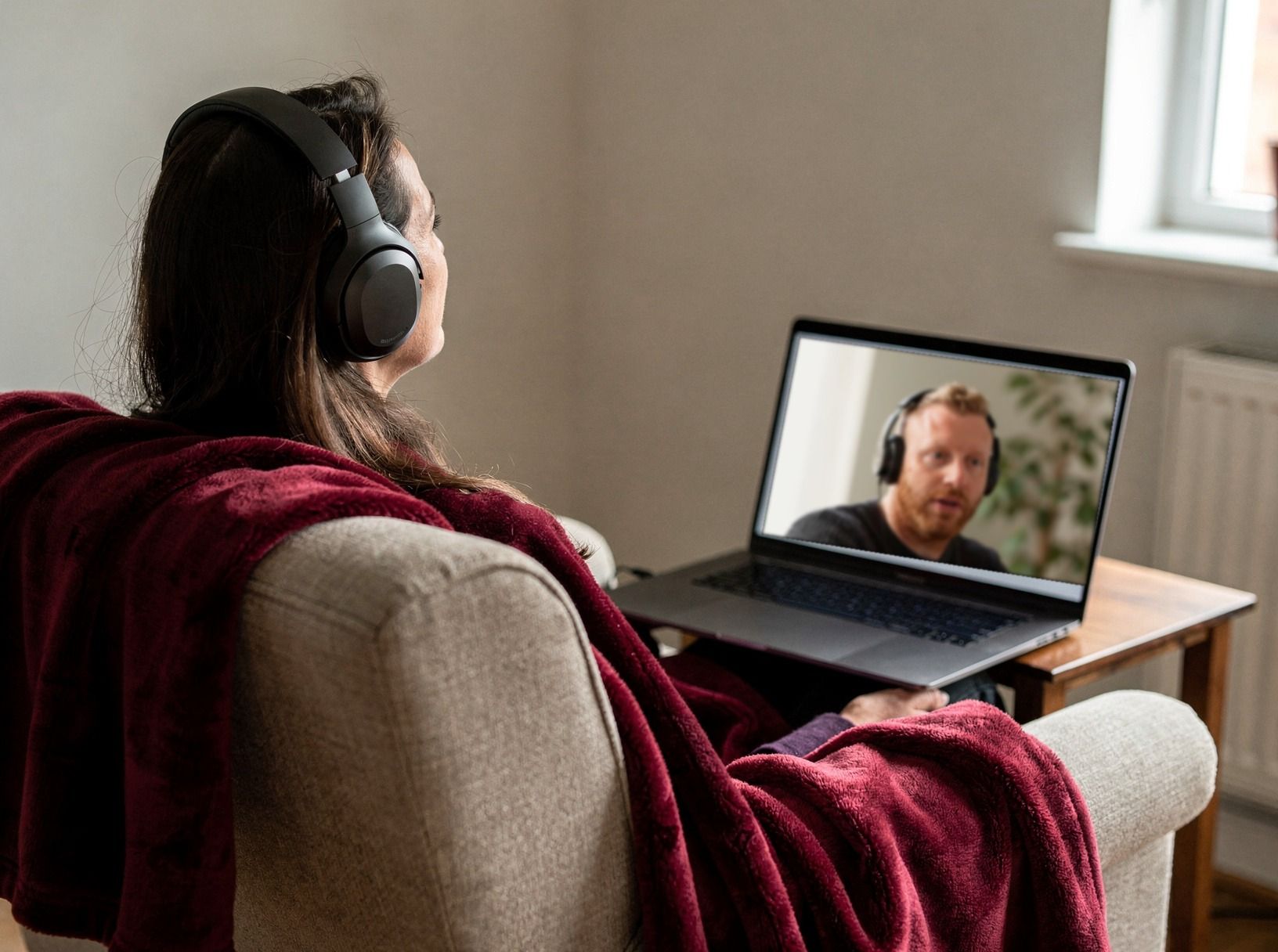 Eine Frau mit Kopfhörern im Sessel, auf dem Laptop vor ihr Tommy Müller im Videocall.